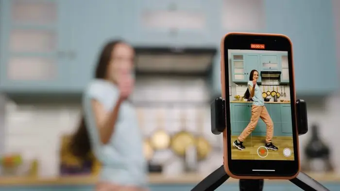 Smartphone on a tripod recording a woman dancing in a kitchen for TikTok content