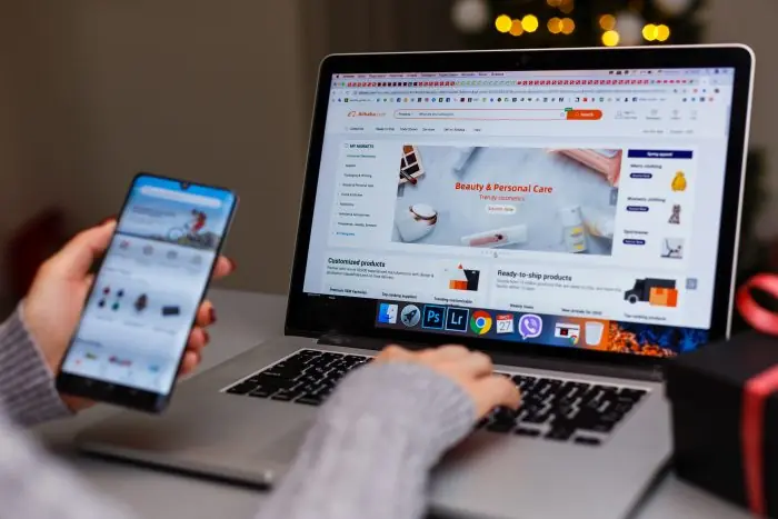 Person holding a smartphone while browsing an online store on a laptop during holiday shopping