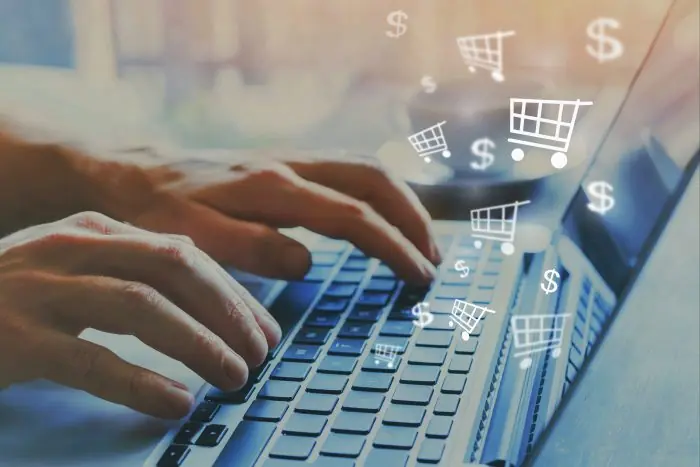Hands typing on a laptop with floating shopping cart and dollar icons for online shopping