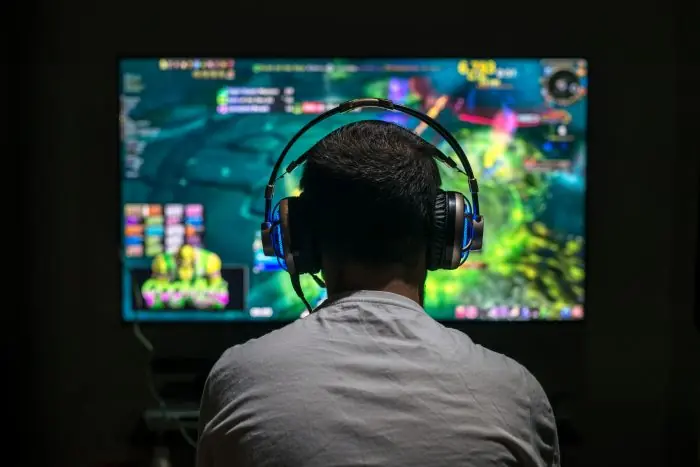 Person wearing headphones playing a video game on a large screen, seen from behind