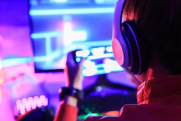 Gamer wearing headphones playing a mobile game in front of a neon-lit screen