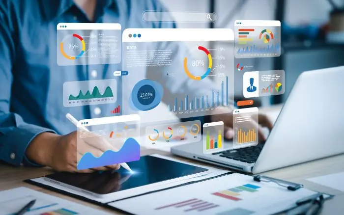 Person using a stylus and laptop with floating analytics dashboards, charts and percentages overlaid