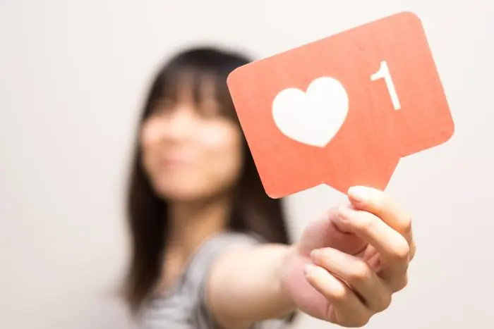 Blurred woman holding out a red social media like notification sign showing a heart and the number 1