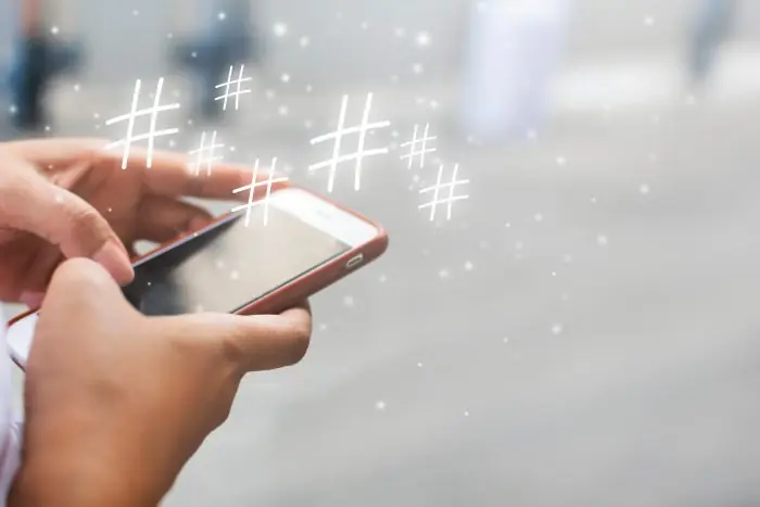 Hands holding a smartphone with hashtag symbols floating above the screen