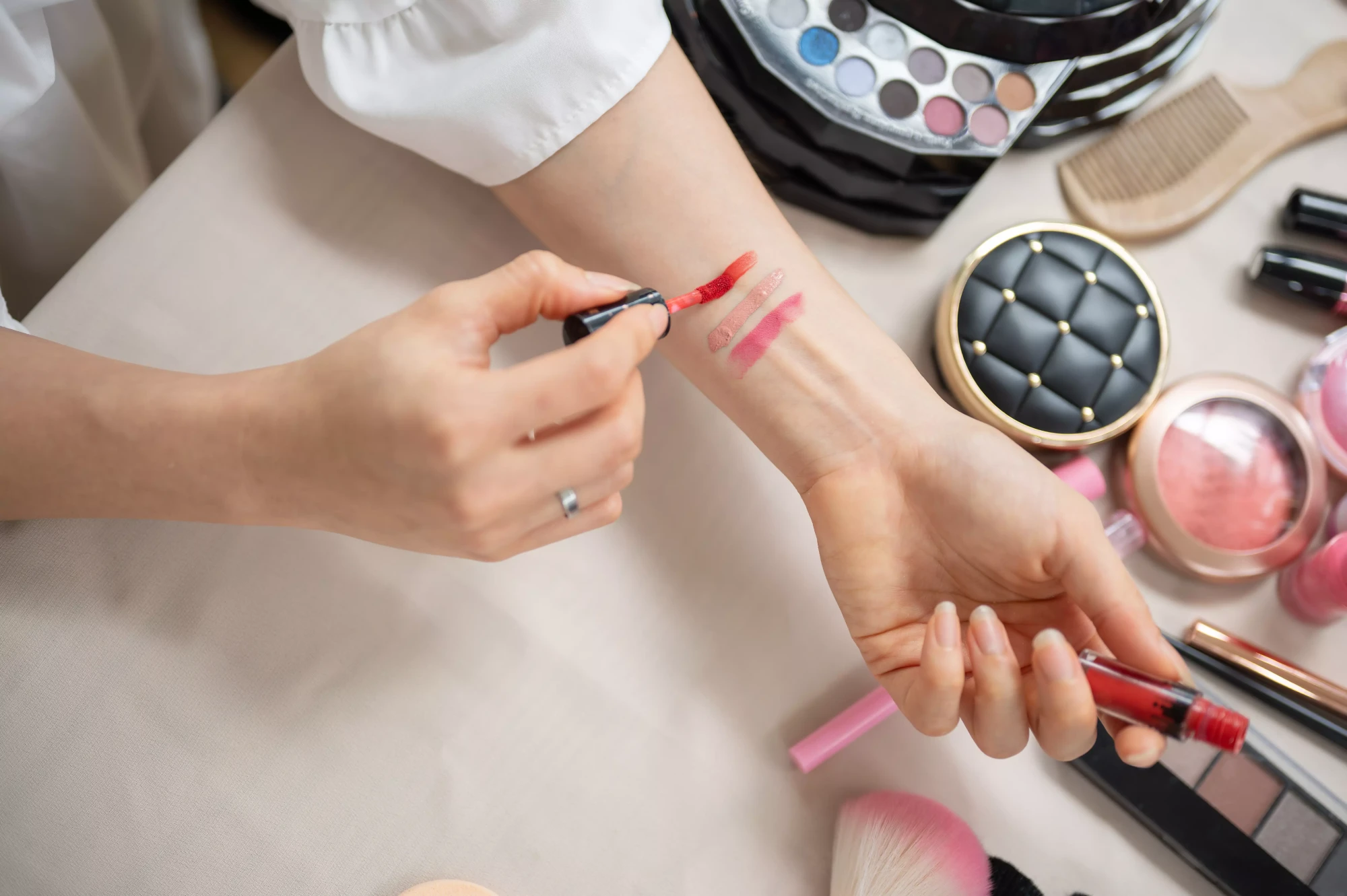 Person swatching lipstick shades on their forearm, surrounded by makeup products