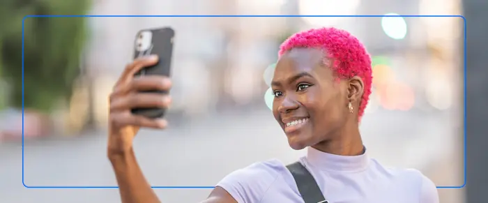 Smiling young woman with short pink hair taking a selfie with her smartphone