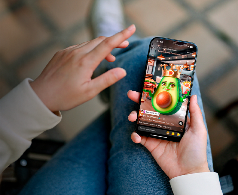 Hands holding a smartphone showing a short video of a crowned avocado character in a Burger King restaurant